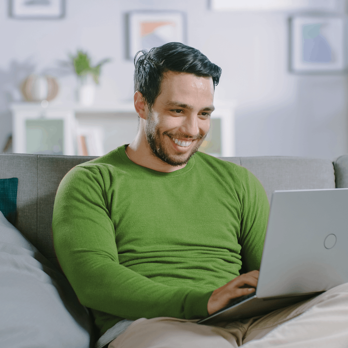 Homem sorrindo sentado no sofá usando um notebook